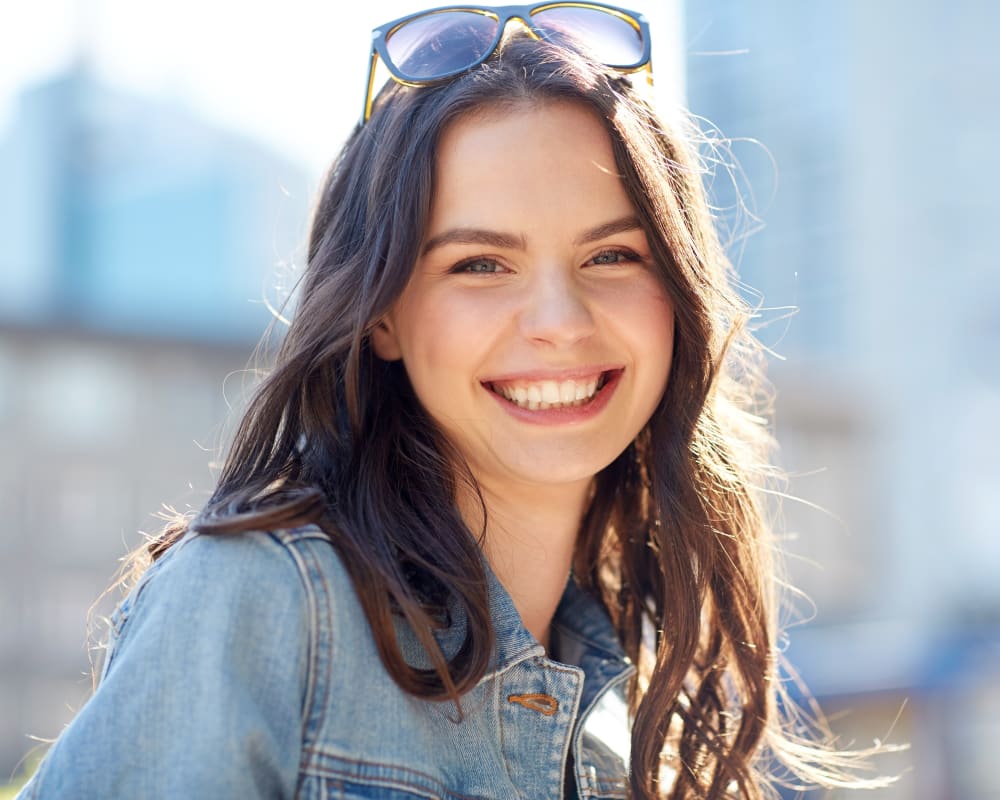 A young teenage girl smiles at the camera. She has sunglasses on her head.