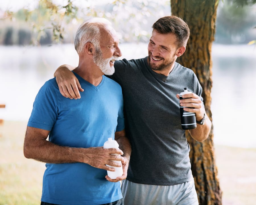 An adult man and a senior man, presumably father and son, are out for a walk by a body of water.